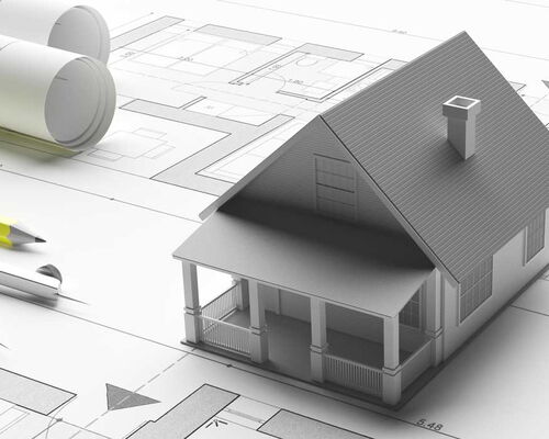 3D Haus steht auf Bauplänen, links liegt ein Zirkel und ein Bleistift.
