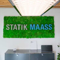 Die Wand eines Büroraumes, es hängt der Schriftzug Statik Maass an der Wand.