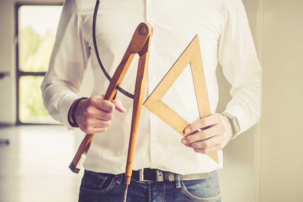 Foto eines Menschen welcher Zirkel und Geodreieck in den Händen hält.